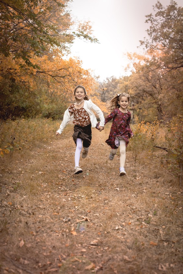 Two sisters running through golden leaves